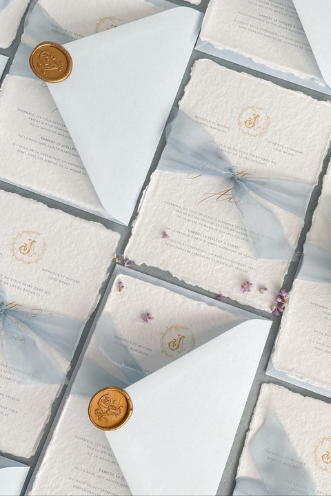 Announce your seaside celebration with a touch of vintage romance and personalization with these unique wedding invitations. Perfect for a beach wedding, this suite is printed on luxurious handmade paper, giving it a soft, textured, and truly premium feel. A bespoke custom vintage letter monogram adds an elegant and personalized touch, while the light sky theme evokes the serene and beautiful atmosphere of the coast.