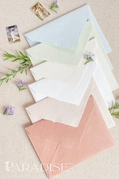 Handmade paper envelopes with wax seals, styled with white flowers and silk ribbon for elegant wedding stationery.