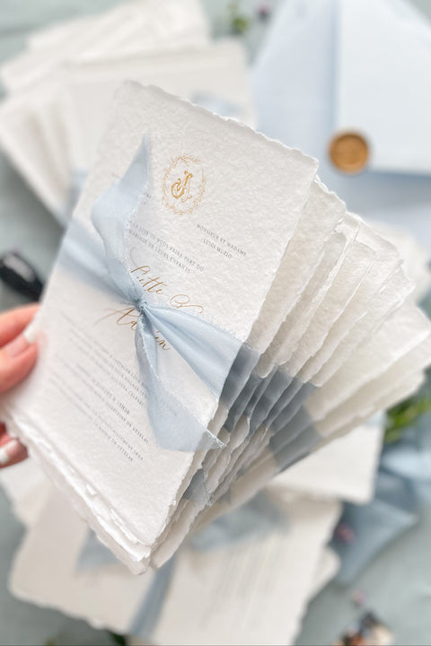 Announce your seaside celebration with a touch of vintage romance and personalization with these unique wedding invitations. Perfect for a beach wedding, this suite is printed on luxurious handmade paper, giving it a soft, textured, and truly premium feel. A bespoke custom vintage letter monogram adds an elegant and personalized touch, while the light sky theme evokes the serene and beautiful atmosphere of the coast.