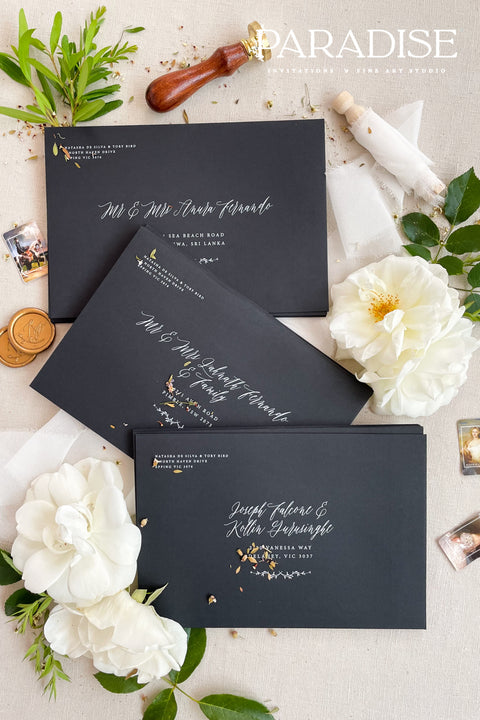 Matte black wedding envelopes with white ink address printing, styled flat lay with florals, wax seal, and greenery, perfect for modern and editorial invitation suites.