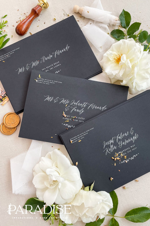 Matte black wedding envelopes with white ink address printing, styled flat lay with florals, wax seal, and greenery, perfect for modern and editorial invitation suites.
