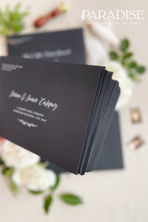 Matte black wedding envelopes with white ink address printing, styled flat lay with florals, wax seal, and greenery, perfect for modern and editorial invitation suites.
