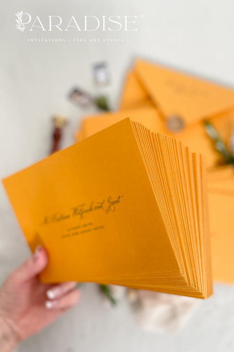 Amber wedding envelopes with printed addresses, styled flat lay with white florals, wax seal, ribbon, and greenery, perfect for warm, elegant invitation suites.