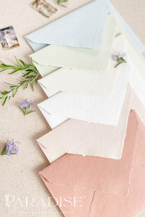 Handmade paper envelopes with wax seals, styled with white flowers and silk ribbon for elegant wedding stationery.
