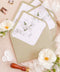 Matcha green wedding envelopes with watercolor botanical liners, styled flat lay with white florals, wax seals, and ribbon for elegant garden invitation suites.