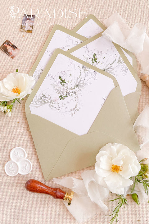 Matcha green wedding envelopes with watercolor botanical liners, styled flat lay with white florals, wax seals, and ribbon for elegant garden invitation suites.