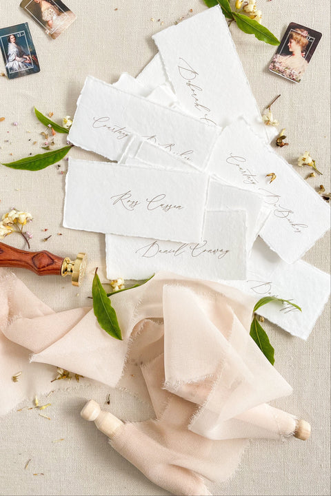 Create a timeless, romantic tablescape with our handmade paper place cards, crafted from luxurious cotton rag paper and finished with natural deckled edges. Each piece features elegant handwritten calligraphy and a soft fine-art texture that complements weddings, intimate dinners, bridal showers, and elevated celebrations. Their artisanal character and organic feel bring warmth, refinement, and delicate charm to any event setting.