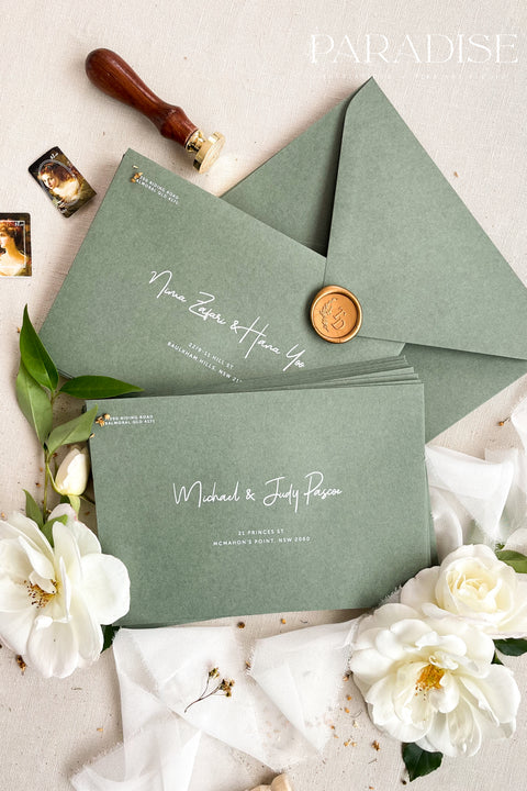 Soft green wedding envelopes with printed addresses, styled flat lay with white florals, greenery, wax seal, and ribbon, perfect for botanical invitation suites.