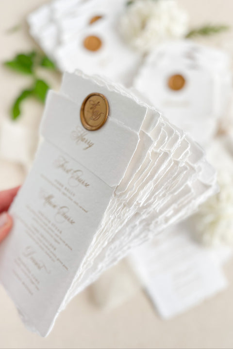 Refine your tablescape with our handmade paper wedding menus with personalized name tags, a luxurious detail that blends artistry and function. Each menu is printed on deckled-edge cotton paper and wrapped in a soft handmade band topped with a vintage gold wax seal - creating a timeless, cohesive aesthetic. Designed for elegant fine-art weddings, these menus double as place cards, adding personalization and charm to every seat.
