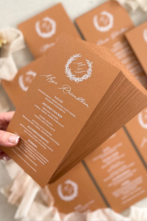 Bring a warm, refined touch to your tablescape with our terracotta wedding menus, designed for couples who love earthy elegance and fine-art craftsmanship. Each menu is printed on premium cardstock in a rich, burnt-clay hue that pairs beautifully with autumnal, bohemian, or rustic wedding palettes. The white wreath monogram adds a timeless detail that unites your stationery suite with your table décor.