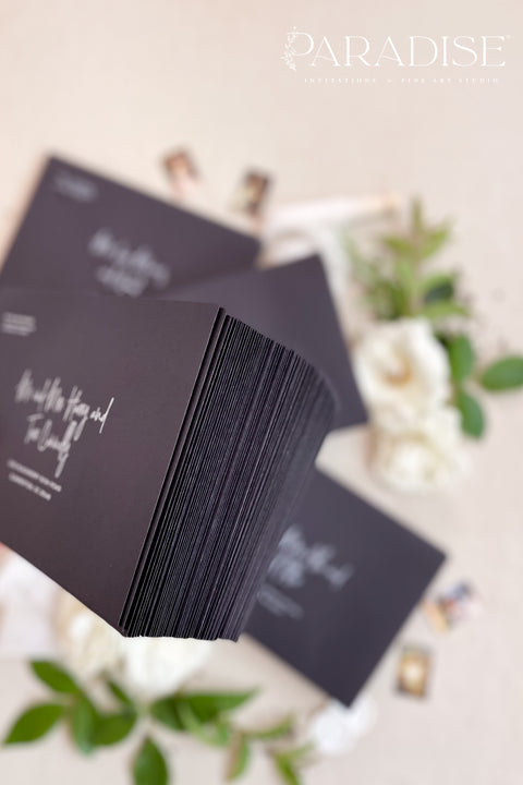 Modern black envelopes with white ink calligraphy printing, photographed flat lay with white flowers, wax seal, and botanical details.