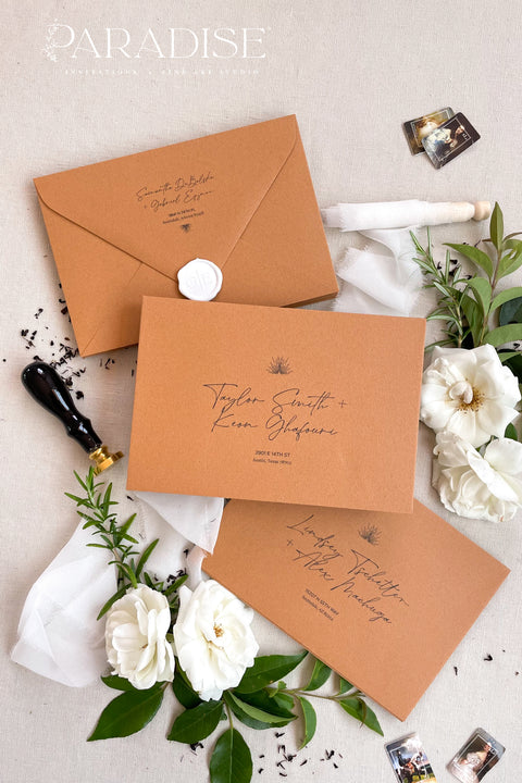 Cinnamon wedding envelopes with printed addresses, styled flat lay with white florals, greenery, wax seal, and ribbon, perfect for warm, elegant invitation suites.