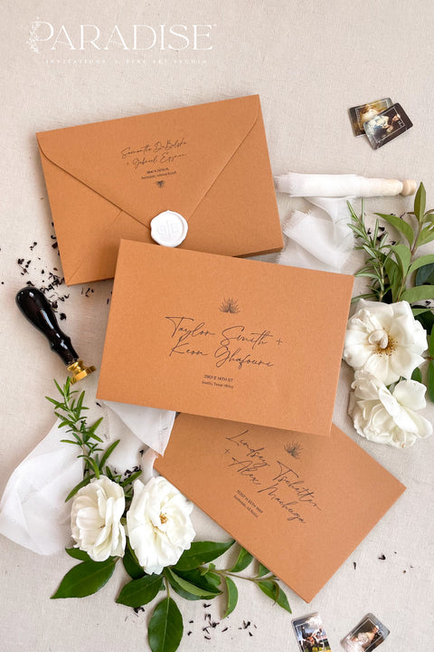 Cinnamon wedding envelopes with printed addresses, styled flat lay with white florals, greenery, wax seal, and ribbon, perfect for warm, elegant invitation suites.
