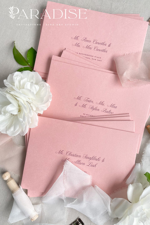 Dusty pink envelopes styled with calligraphy, silk ribbon, and flowers for elegant wedding stationery.