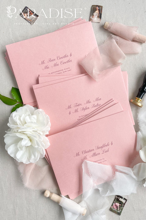 Dusty pink envelopes styled with calligraphy, silk ribbon, and flowers for elegant wedding stationery.