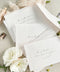 Minimalist white wedding envelopes with black ink printing, styled with botanical accents and ribbon for timeless, modern invitation suites.