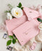 Dusty pink envelopes with custom address printing, displayed on a surface with a white rose and green leaves, indicating a possible use in wedding or formal invitation settings.