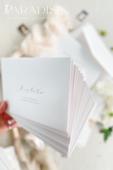 Minimalist white wedding envelopes with black ink printing, styled with botanical accents and ribbon for timeless, modern invitation suites.
