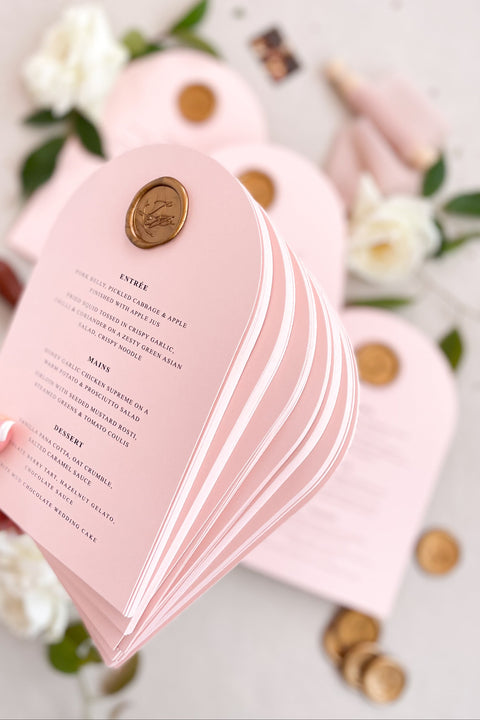Bring a touch of modern romance to your wedding tables with our arched blush menus, adorned with luxurious gold wax seals and elegant typography. Crafted from premium cardstock in soft pink tones, these menus exude sophistication and charm - perfect for fine art, modern, or romantic weddings. Each piece combines timeless craftsmanship with contemporary design, creating a refined focal point for your reception tables.