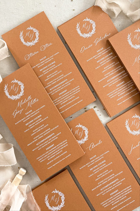 Bring a warm, refined touch to your tablescape with our terracotta wedding menus, designed for couples who love earthy elegance and fine-art craftsmanship. Each menu is printed on premium cardstock in a rich, burnt-clay hue that pairs beautifully with autumnal, bohemian, or rustic wedding palettes. The white wreath monogram adds a timeless detail that unites your stationery suite with your table décor.
